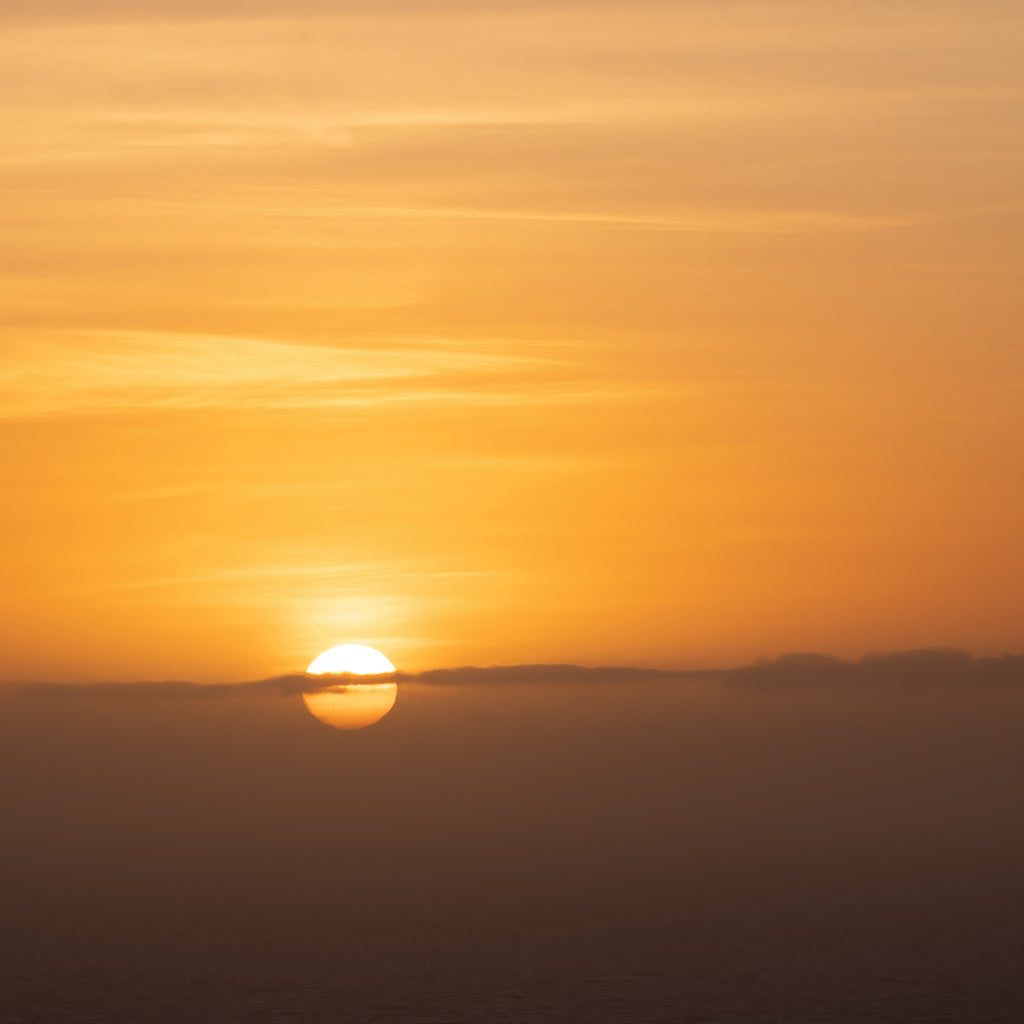 The sun highlights low clouds on the horizon during a spectacular sunrise over the ocean near Freycenet in Tasmania, Australia. As an added bonus I also captured a pair of sunspots in the image.