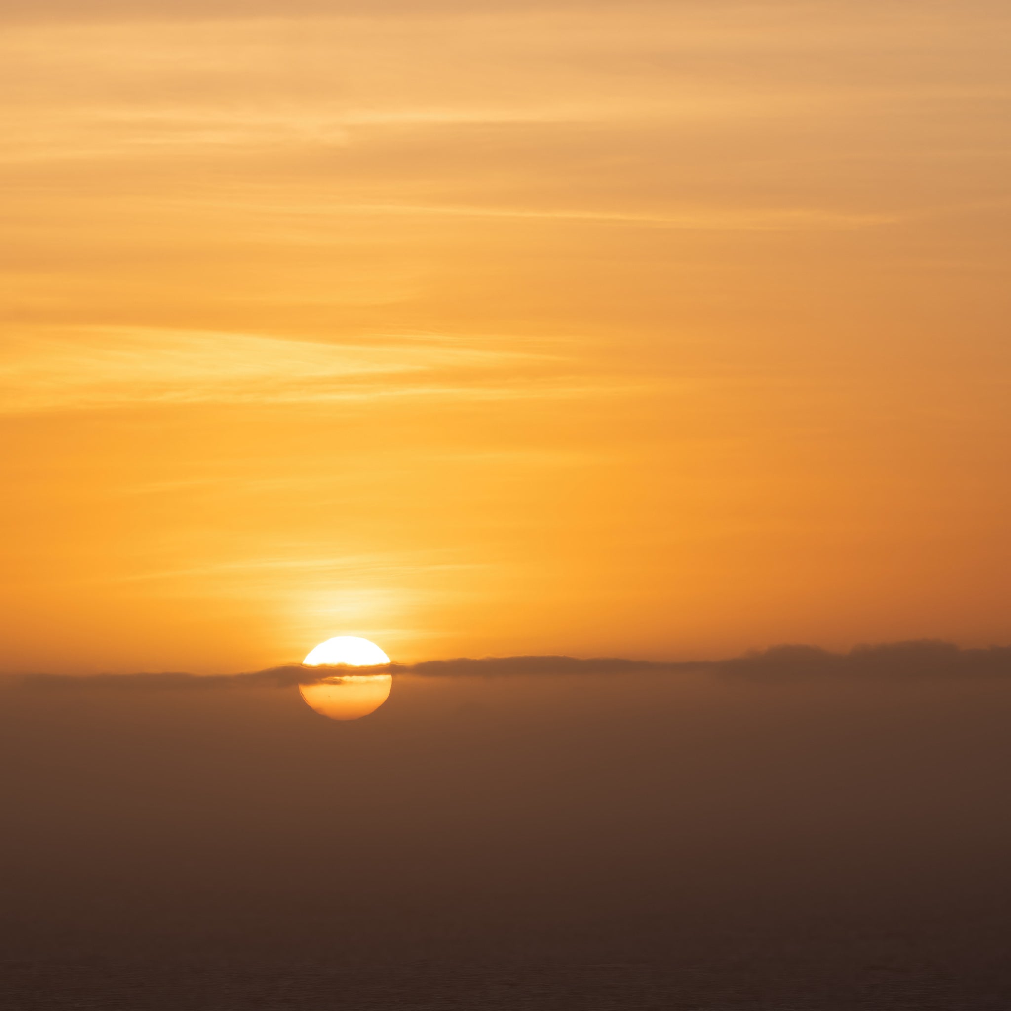 The sun highlights low clouds on the horizon during a spectacular sunrise over the ocean near Freycenet in Tasmania, Australia. As an added bonus I also captured a pair of sunspots in the image.