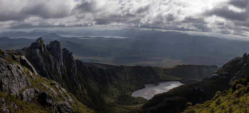 Beautiful Lake Neptune glinting in the early morning sun as the clouds above produce ethereal rays lighting the crags and hillsides all around. Taken from atop the Western Arthurs in Tasmania, Australia.