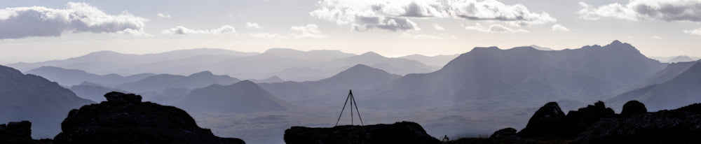 An amazing panorama capturing the essence of Out Under The Sky. My tripod is silhouetted against a back drop of mountain ranges fading to the horizon in silver afternoon light which lights the clouds from above. One of my favourites. Taken from atop the Western Arthurs in Tasmania, Australia.