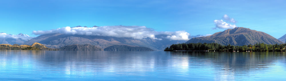 Early morning sunlight lights up the clouds resting on the hilltops surrounding Lake Wanaka on the South Island of New Zealand.